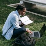 Writer working on a laptop and notebook while sitting outdoors in a park