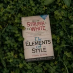The Elements of Style by William Strunk Jr. and E. B. White resting on a bed of green clover and foliage.